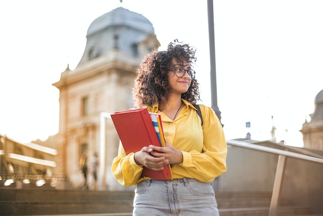 Woman in a yellow shirt smiling and holding books.